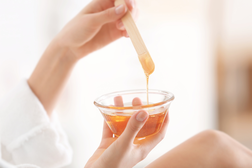 Woman holding bowl with hot wax on blurred background